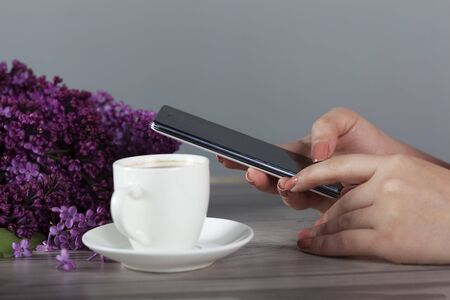 woman hand phone and coffee with lilac on the tableの写真素材