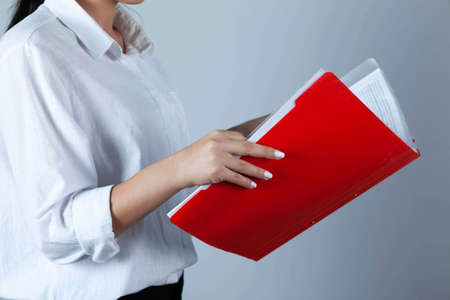 A young girl stands near the shelf and holds a red folder in her handsの写真素材