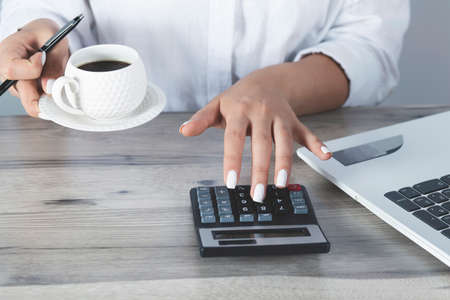woman hand cup of coffee and calculator on the deskの写真素材