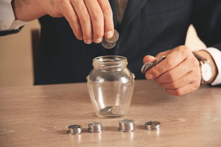 businessman hand holding coins putting in jar concept finance and accounting savingの写真素材