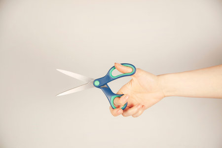 woman hand holding blue scissors on gray background