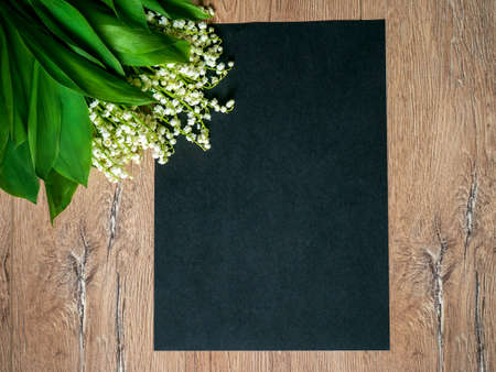 Bouquet of lilies of the valley on a wooden background and an empty piece of black paper.の写真素材
