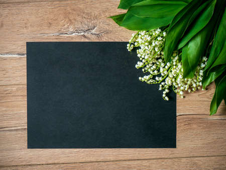 Bouquet of lilies of the valley on a wooden background and an empty piece of black paper.の写真素材