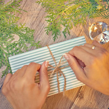 Christmas gift in hands, pine cones, thuja branches on wooden background. Flat lay, top view, copy space.の写真素材