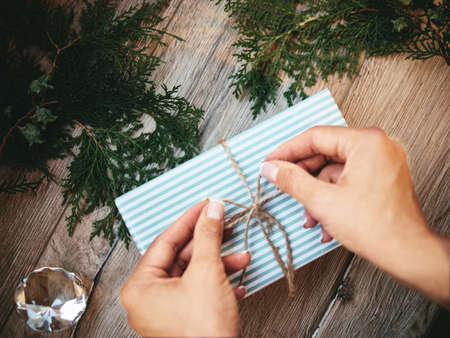 Christmas gift in hands, pine cones, thuja branches on wooden background. Flat lay, top view, copy spaceの写真素材