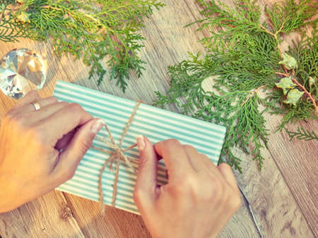 Christmas, winter, new year concept. Hands with Gift for holidays. Gifts, different winter plants on wood background. Flat lay, top viewの写真素材