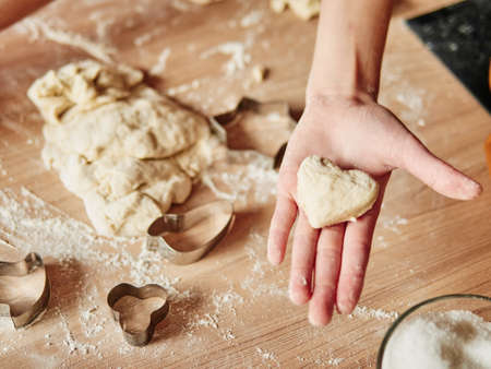kids hands holding dough in heart shape top view. Baking ingredients on the dark wooden table.の写真素材
