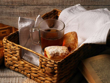 Tea and sweet cookies in a wicker tray on white wooden background. Open Book near the afteroon tea.の写真素材