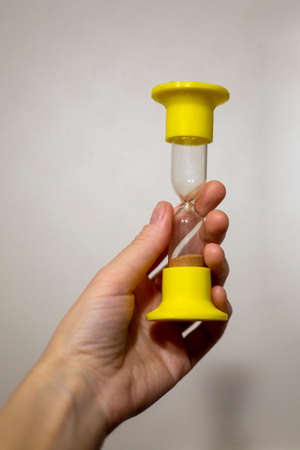 Yellow hourglass with spilled sand in a woman's hand on a gray backgroundの写真素材