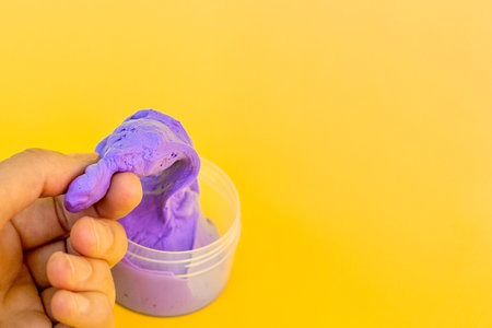 A woman's hand crumples purple rubber taken out of a jar on a bright yellow background. Anti-stress...
