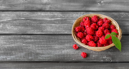 Fresh raspberries with a leaf in a wicker basket on a wooden table. Banner. Space for text. copy...