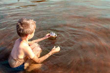 a boy with a hemangioma on his back is swimming and playing in a small yacht with sails. The concept of summer games with waterの写真素材