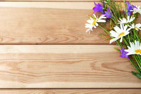 A bouquet of flowers of bluebells and daisies on a light wooden background. Congratulations. Holiday. Birthday. A flat copy space with a top viewの写真素材
