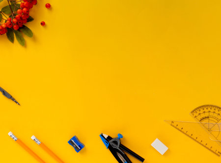 Yellow background with rowan berries and stationery. The concept of Back to School. Pencils, eraser,...