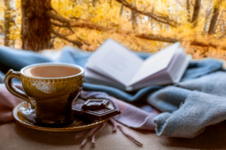 The idea of coziness, hugge, home comfort. Autumn light sadness. Coffee, chocolate, a blanket and a book on the background of a forest landscape on an autumn eveningの写真素材