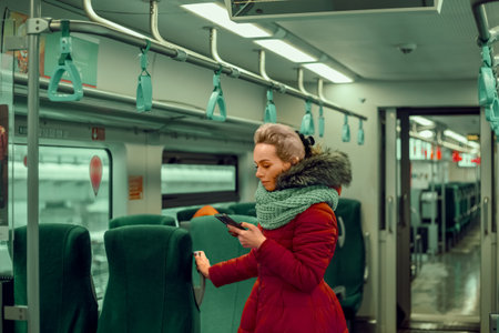 A young woman in winter clothes of the trendy vivid magenta color with a fur collar is talking via video link in the subway.の写真素材