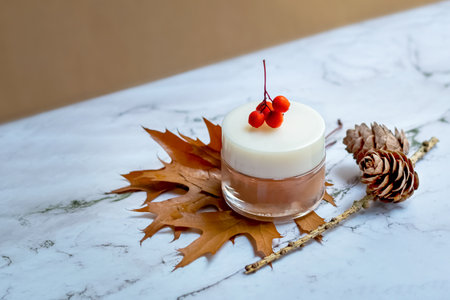 A jar of face cream on the background of autumn leaves, berries and cones. Mockupの写真素材
