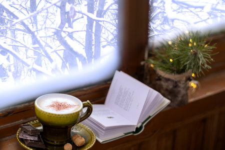 Coffee, chocolate and a book by the window with snow-covered trees. Winter lifestyle, hugge.の写真素材