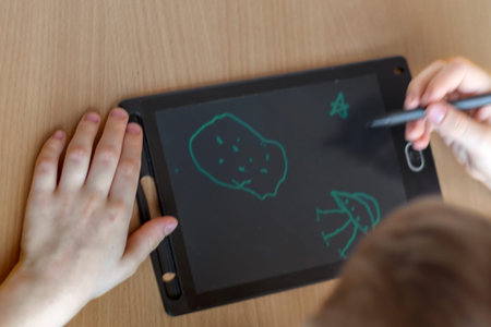 An unrecognizable boy draws with stylus on graphics tablet on theme of space. Top view, close-up.