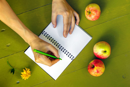 Woman writes down plans for fall in an empty notebook. Nearby on table are ripe apples and autumn...
