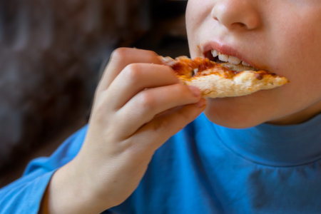 Child takes bite out of slice of pizza. Close-up. An unrecognizable person