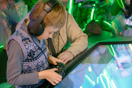 Boy wearing headphones and holding gamepad with his father explores technology on an interactive...