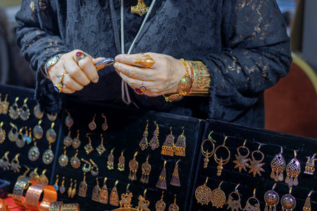 Close-up of female artisan skillfully creating jewelry with tongs, surrounded by handmade gold and silver accessories.