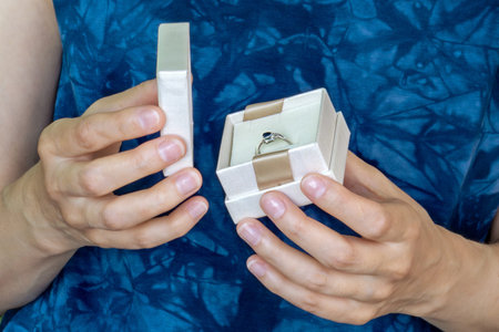 Close-up of woman's hands opening small, elegant gift box containing blue stone ring.