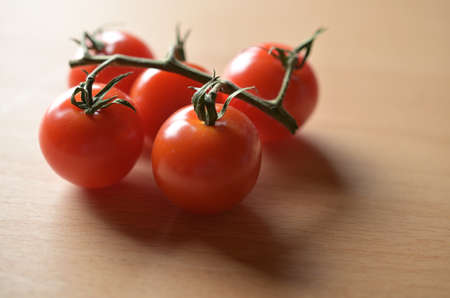 Fresh tomatoes on a branch, on a new wooden table.の写真素材
