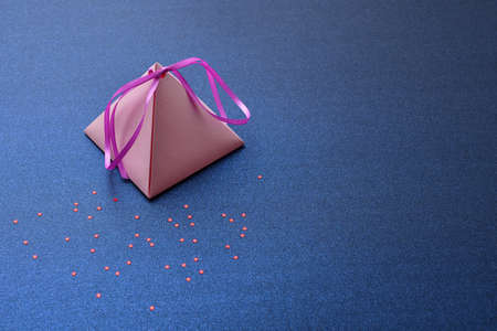 Holiday card, with a pink pyramidal gift box on a blue silver background with red stars, space for text. Festive background for Valentine's Day, International women's day, Christmas and New year.の写真素材
