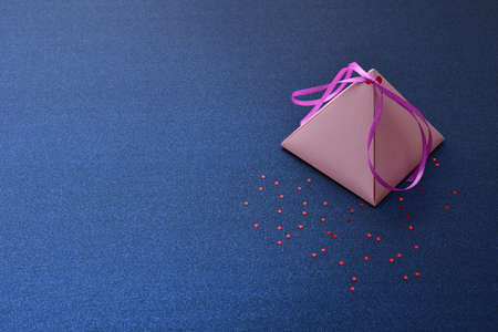 Festive background for Valentine's Day, International women's day, Christmas and New year. Holiday card, with a pink pyramidal gift box on a blue silver background with red stars, space for text.の写真素材