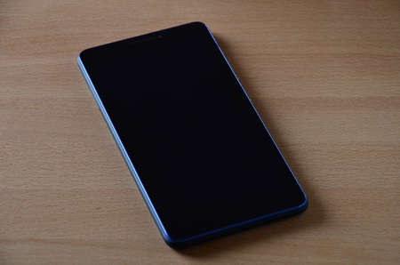Tablet computer with a blank black screen for your project and space for text, isolated on an office wooden table.の写真素材