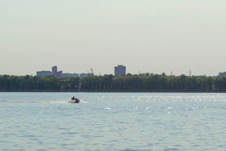 Summer, heat. A woman is riding a water scooter down the river. The city is seen from behind