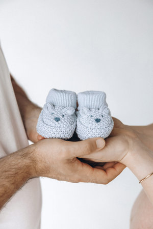 A cropped image of a man and woman holding baby booties against a white background.