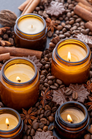 Soy scented candle in a jar. Coffee beans, anise, cinnamon spices. The candles are burning. Dark background.の写真素材