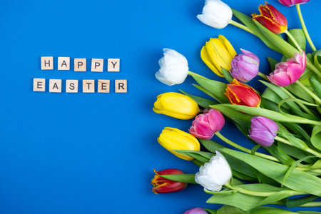 Bouquet of multi-colored tulips on a blue background. Happy Easter phrase. Spring Flower. Festive...