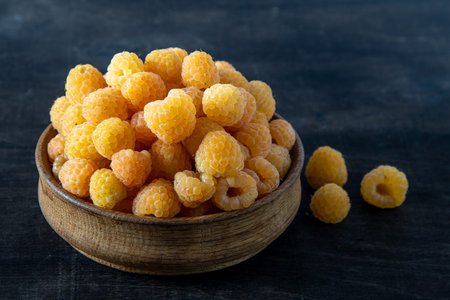 Yellow raspberries in a wooden bowl on the table. Summer berries background. Vitamin food, berry...