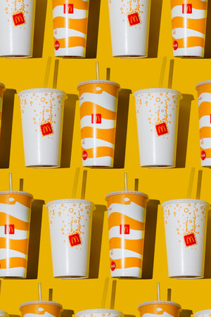 Yellow glass of McDonalds. Paper cup with lid. Takeaway drink. McDonalds logo. McCafe cup shadow top view pattern. Orange juice Fanta drink Fastfood yellow background Ukraine, Kyiv - October 6, 2023のeditorial素材