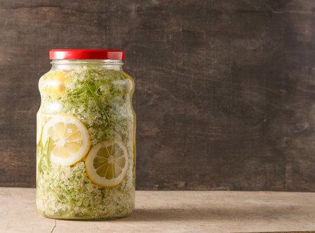 Elder flowers drink juice glass. White flower and lemon. Harvesting buds for making syrup and drink at summer. Cooking and food on the table. Sambucus plant in jar.の写真素材