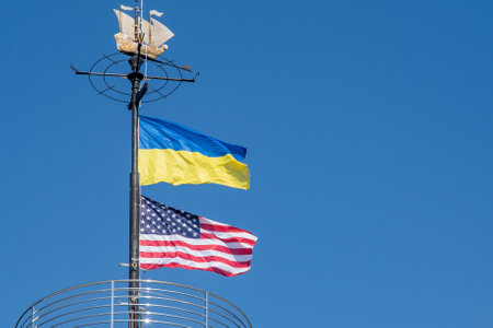The flags of Ukraine and the USA flutter on a flagpole against a blue sky. State symbol. Ukrainian blue and yellow flag. Wind day outdoor.の写真素材