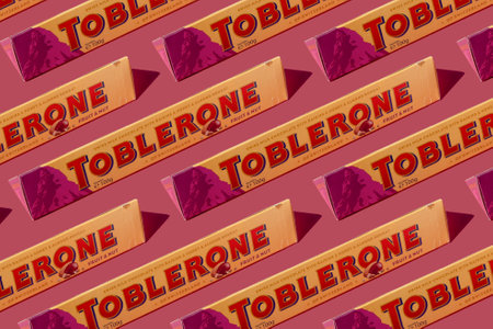 Toblerone Swiss chocolate bar with nuts. New package with mountain logo on pink background. Candy sweets are a classic souvenir from Switzerland. Kyiv, Ukraine - July 10, 2023.のeditorial素材
