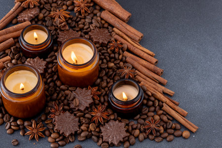 Soy scented candle in a jar. Coffee beans, anise, cinnamon spices. The candles are burning. Dark background.の写真素材