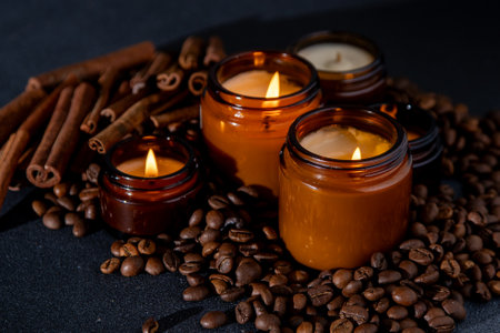 Soy scented candle in a jar. Coffee beans, anise, cinnamon spices. The candles are burning. Dark backgroundの写真素材