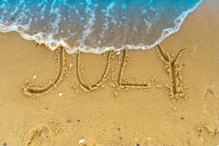 The word July is written on the sand of a beach by the sea. Washed off by a wave.の写真素材