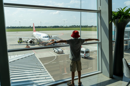 At the ODS airport await departure. The plane is outside the window. A child is looking at the plane through the terminal window. A boy passenger expects a journeyのeditorial素材