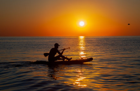 Silhouette of a man floating on a board with an oar. Dawn sun on the sea. Swimming on a supboard. Water active sports. Beautiful landscape. Sunset on the sea. Ocean coast. Copy space.の写真素材