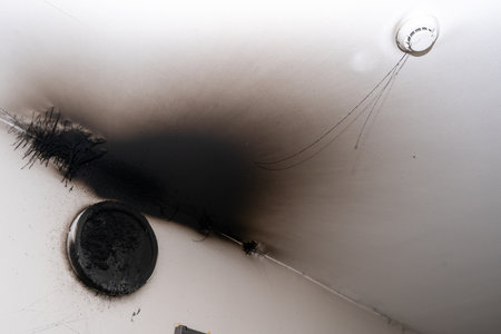 Burnt out LED lamp and smoke detector on ceiling showing fire damage and soot marks.の写真素材