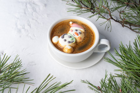 Cup of coffee with marshmallows. Marshmallow snowman in a Santa Claus hat. Winter drink in the snow. Christmas tree. Top viewの写真素材