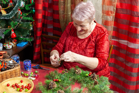 Senior old woman craft. Grandmother make Christmas wreath from spruce branches. Home decoration in Decemberの写真素材