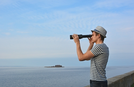 Young man is looking through the spyglass at the seaの写真素材